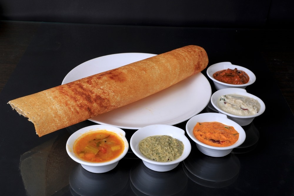 Masala Dosa served with sambar and assorted chutneys, featuring a crisp golden exterior and rolled presentation
